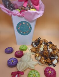 Chocolate covered caramel popcorn chocolate flower pop and chocolate foiled daises in a gift box.