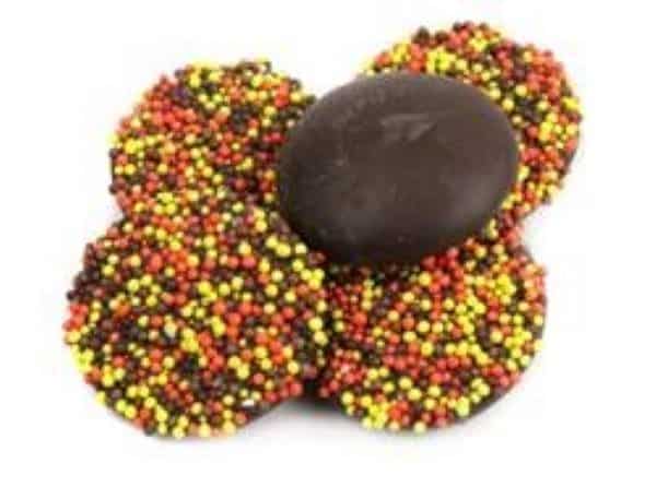 Round disks of chocolate topped with colorful nonpareils in orange, brown, and yellow.